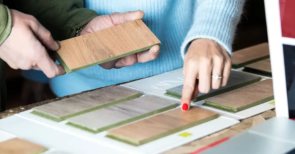 Unrecognizable craftsman helping female client in picking sample for order during work at workbench in joinery