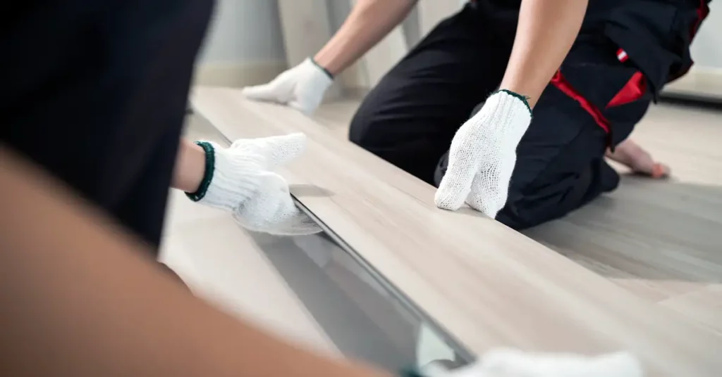 Close-up of Craftsman worker installs laminate board on floor at home.